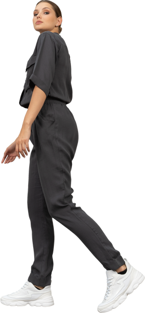 Side view of a walking young woman in a jumpsuit looking at camera