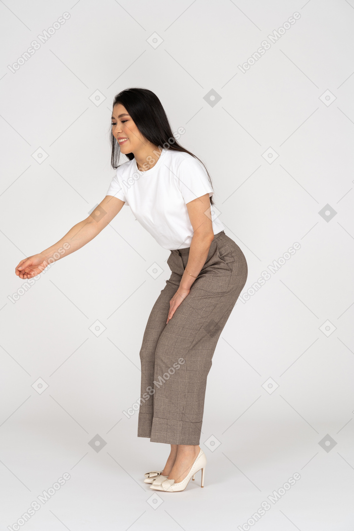Vista lateral de una joven en pantalones y camiseta extendiendo su mano y agachándose
