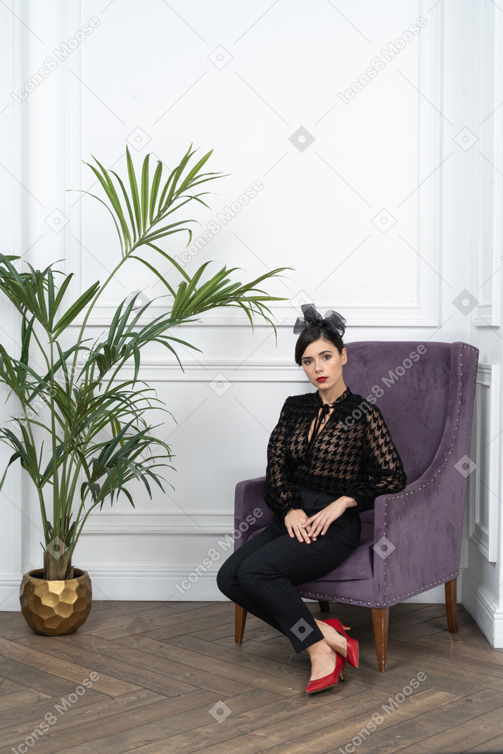 A woman in black outfit sitting on an armchair next to a potted plant