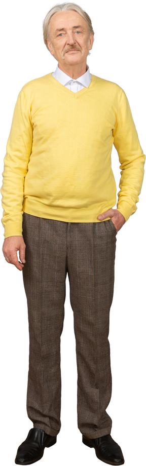 Front view of a displeased old man wearing yellow pullover and putting hand in pocket and looking at camera