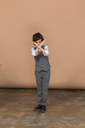 Vista frontal de um menino bonito de terno cinza, mostrando o sinal de pare