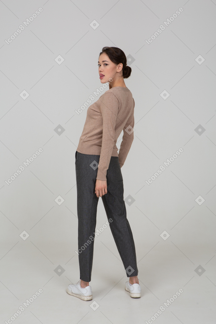 Three-quarter back view of a young lady in pullover and pants showing tongue