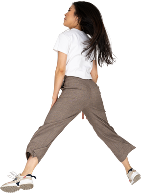 Vista posteriore di una giovane donna che salta in calzoni e t-shirt allargando le gambe