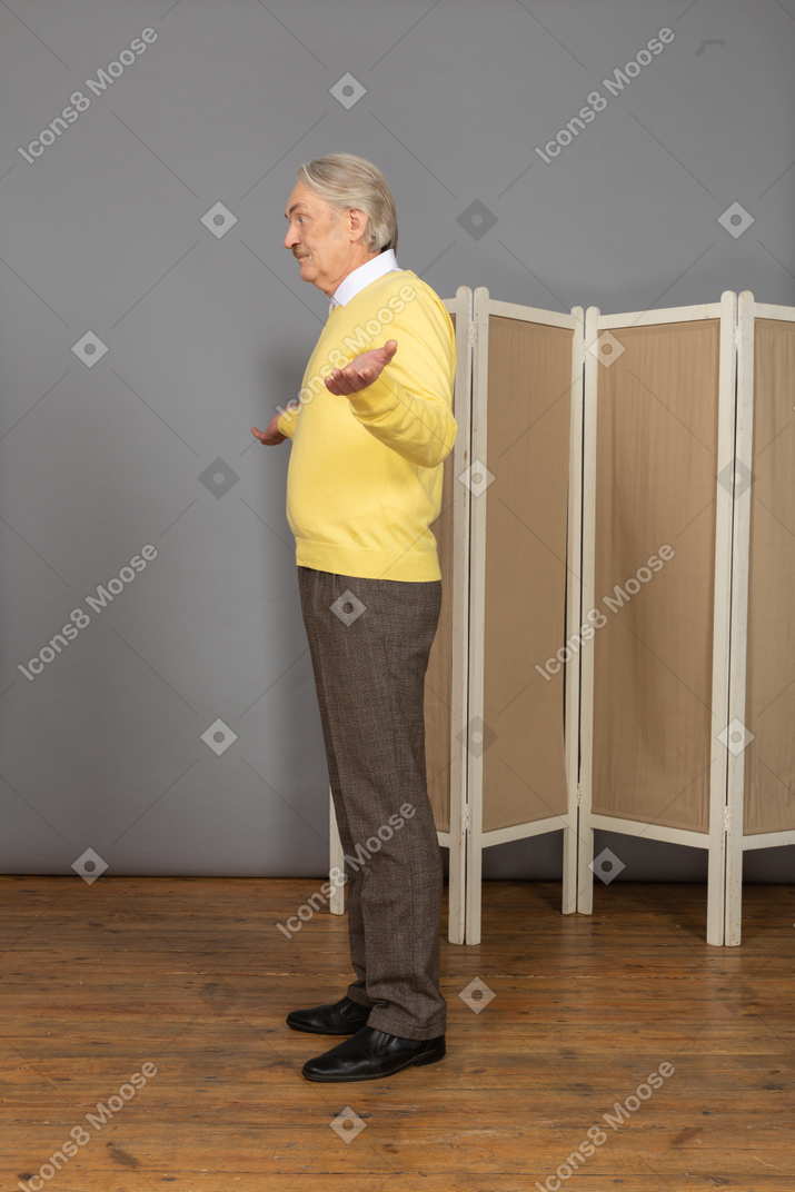 Side view of a perplexed old man raising hands looking aside