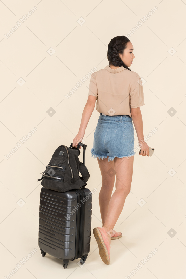 Vue arrière d'une jeune voyageuse avec valise