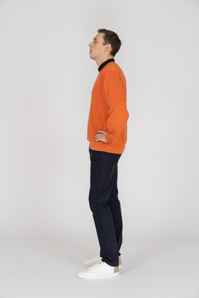 A man in an orange sweater stands in front of a white background
