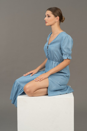 Vista laterale della giovane donna in abito blu seduto su un cubo