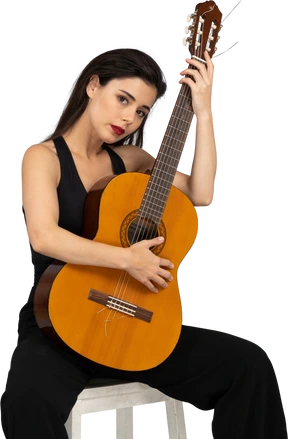 Front view of a sitting young lady in black suit embracing her guitar