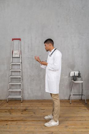 Vista lateral de um jovem médico em uma sala com escada e cadeira explicando algo