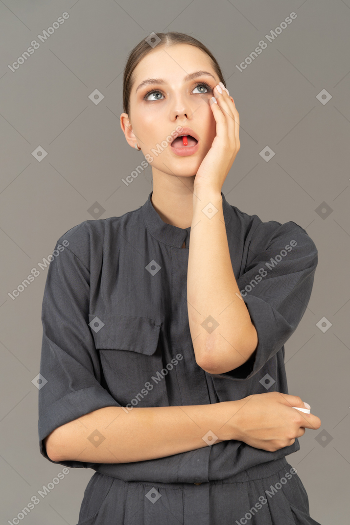 Vue de face d'une jeune femme en combinaison tenant une pilule sur sa langue