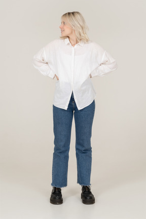 Front view of a blonde female in casual clothes putting hands on hips and looking to the left