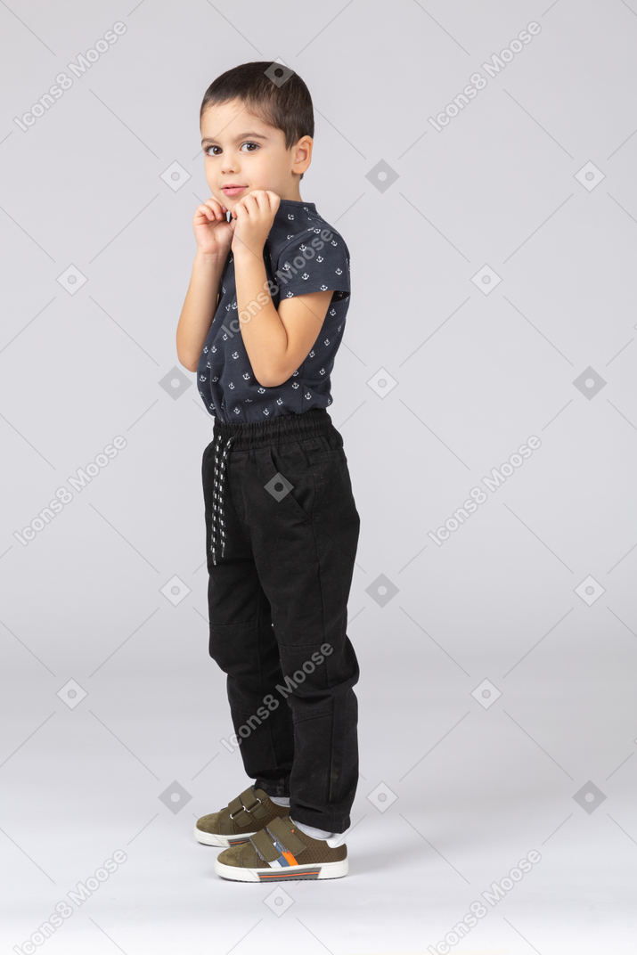 Side view of a scared boy posing with hands on chin and looking at camera