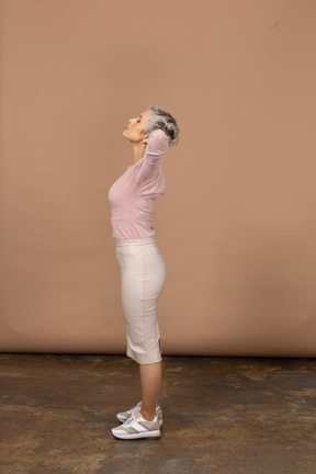 Vista lateral de uma mulher com roupas casuais em pé com as mãos atrás da cabeça