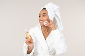 Black woman in white bathrobe and head towel enjoying her skin care routine