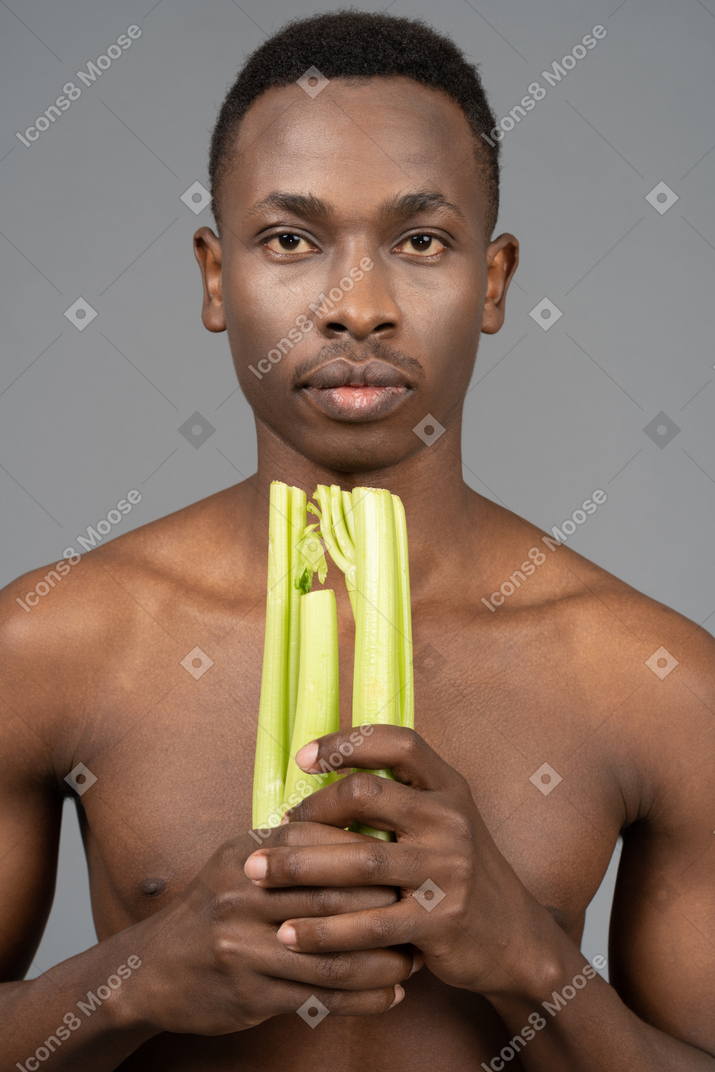 A shirtless young man holding a celery