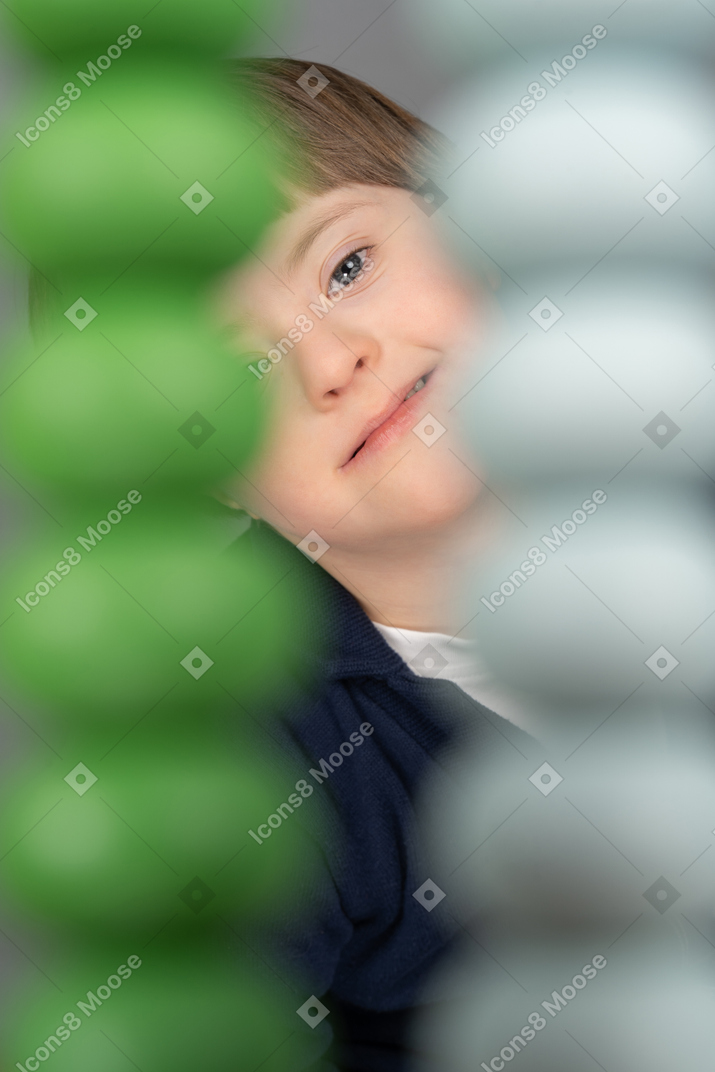 Kleiner junge, der kamera durch graue und grüne perlen betrachtet