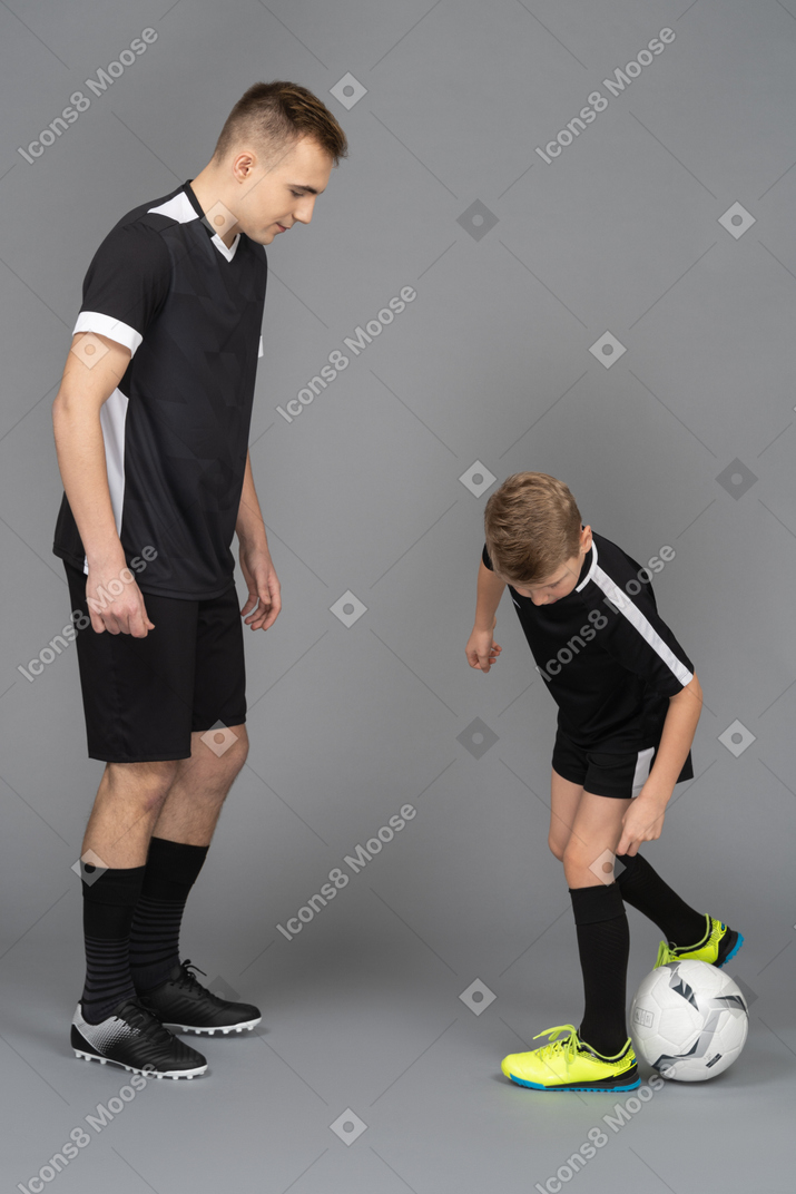 De cuerpo entero de un joven entrenando a un niño pequeño cómo jugar fooyball