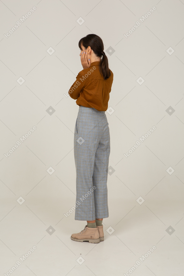 一位身着马裤和衬衫的年轻亚洲女性的四分之三后视图抚摸她的脸