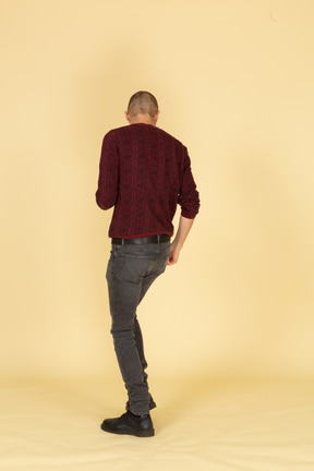 Back view of a dancing young man in red pullover raising leg