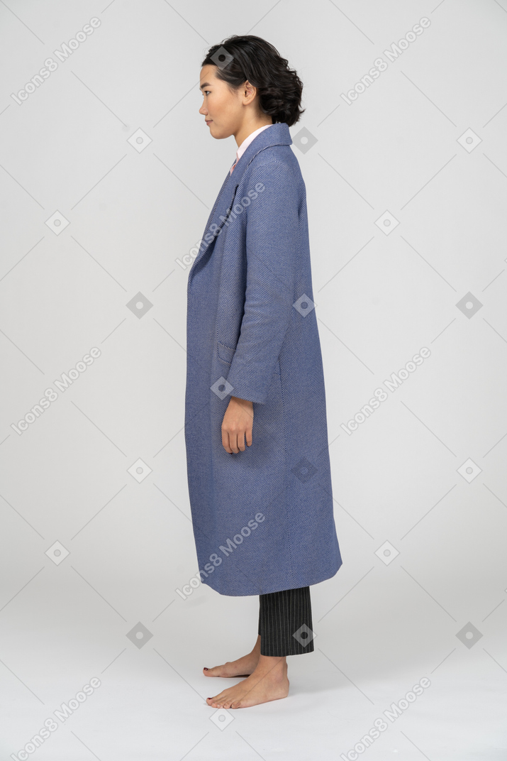 Вид сбоку на женщину в синем пальто, стоящую с руками по бокам