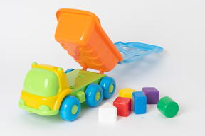 A colorful toy dump truck and some kids' cubes of many colours lying against a plain white background