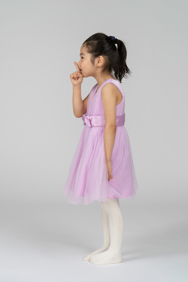 Side view of a little girl in a pretty dress showing silence sign