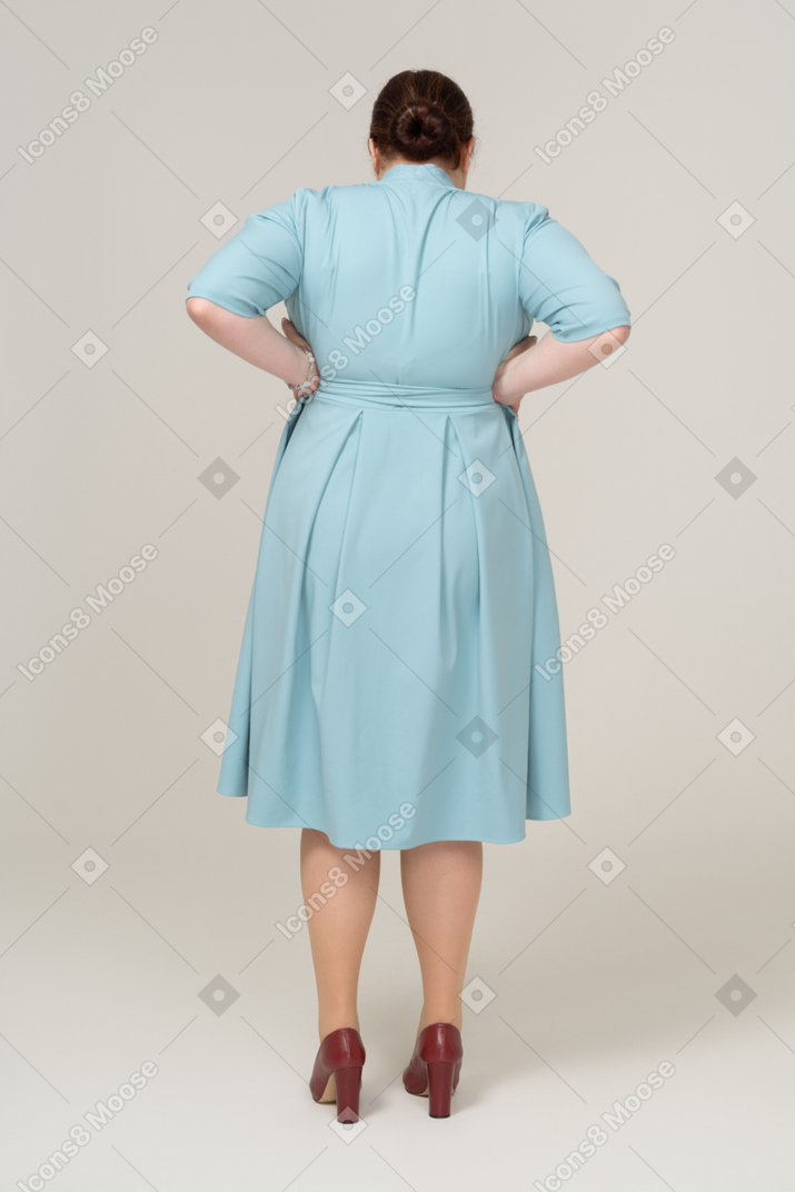 Вид сзади женщины в голубом платье, стоящей с руками на бедрах