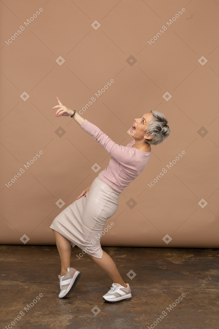 Vista lateral de uma mulher emocional em roupas casuais, curvando-se e apontando com o dedo