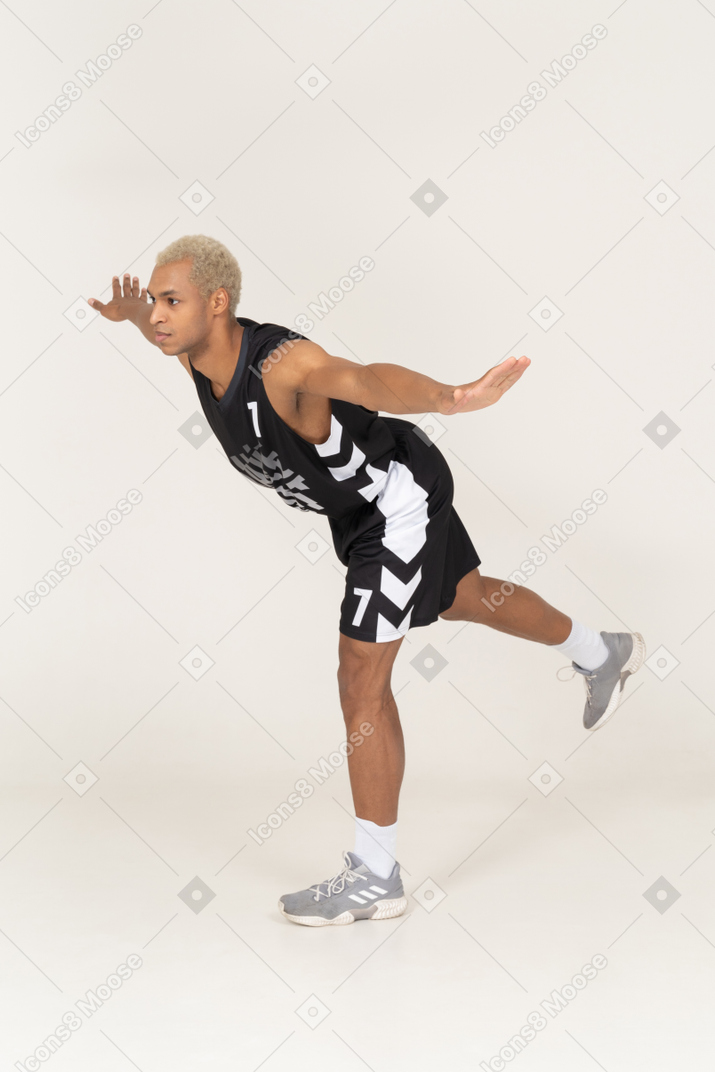 Vista de tres cuartos de un joven jugador de baloncesto masculino de equilibrio inclinado hacia adelante y de pie sobre una pierna