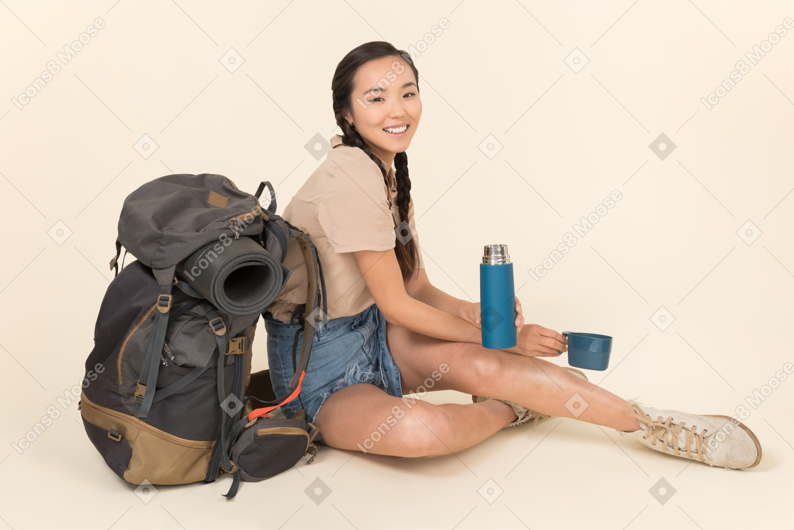 Junge asiatische frau, die nahe rucksack sitzt und thermosflasche behandelt