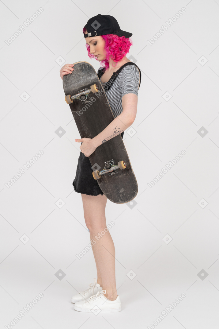 Girl with curly pink hair holding a skateboard