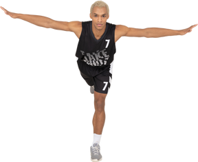 一个平衡的年轻男篮球运动员向前倾斜 & 站在一条腿上的前视图