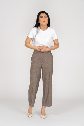 Vista frontal de una joven en pantalones y camiseta tocando su estómago