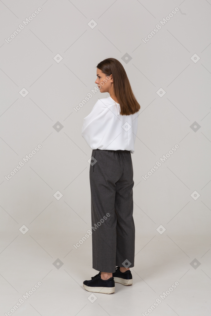 Three-quarter back view of a serious young lady in office clothing looking aside