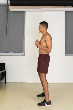 Standing in profile young man in sport shorts biting jumping rope