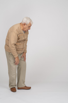 Vista lateral de un anciano con ropa informal agachándose