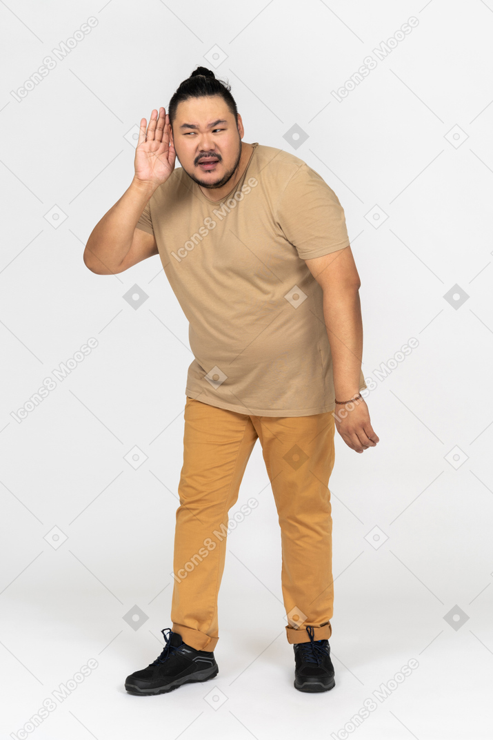 Molesto hombre asiático ayudando a sí mismo con su palma tratando de escuchar algo
