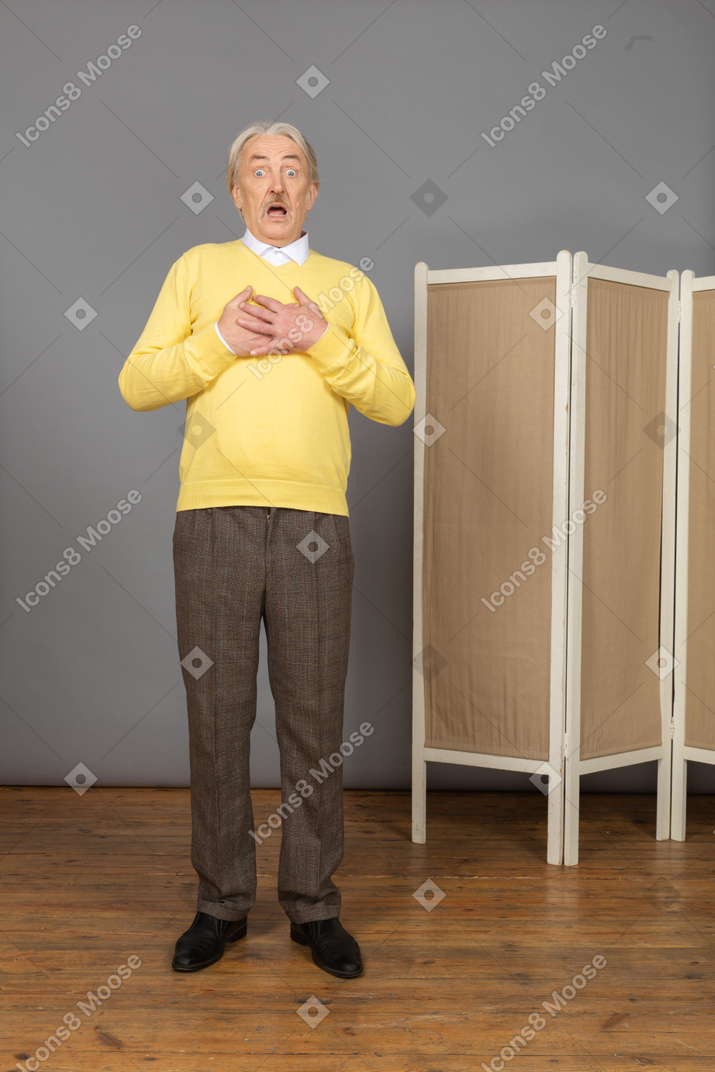 Front view of an astonished old man touching chest