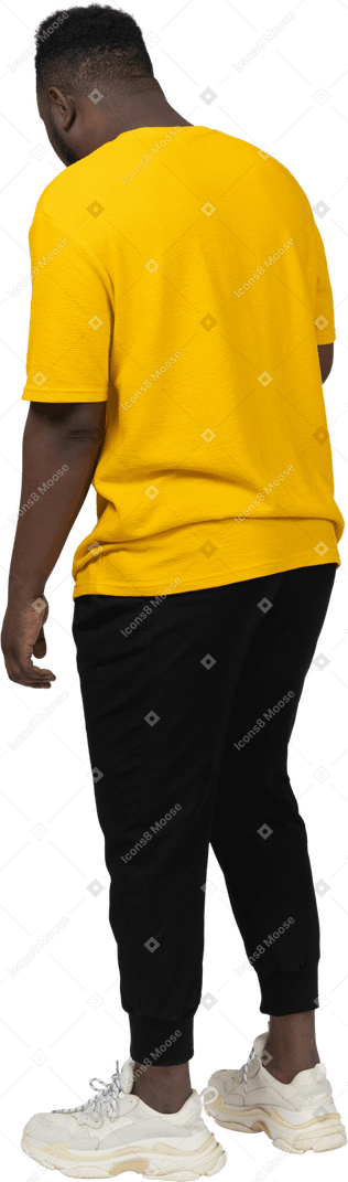 Vista posteriore di tre quarti di un giovane uomo dalla pelle scura in maglietta gialla che sta fermo