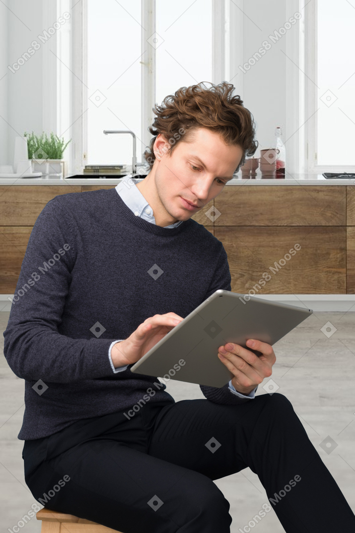 A man sitting on a stool looking at a tablet