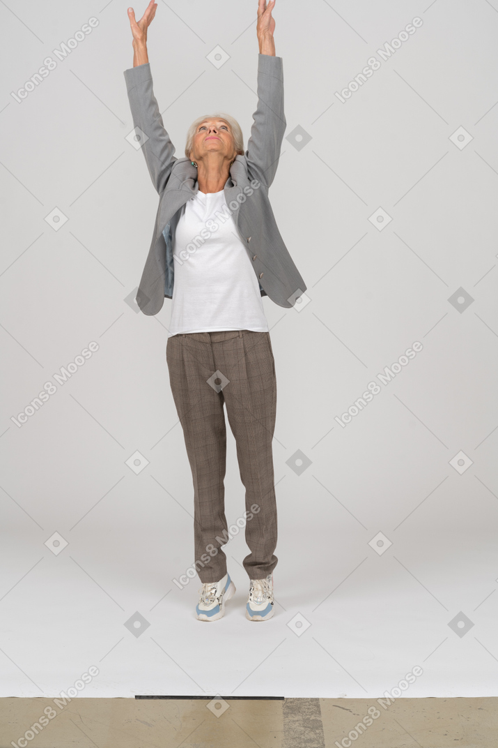 Вид спереди старушки в костюме, стоящей на цыпочках и поднимающей руки