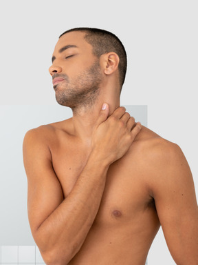 A shirtless man holding his neck in pain