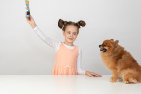 Ребенок девочка показывает пачку собаке угощение шпиц