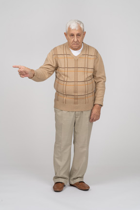 Vista frontal de un anciano con ropa informal apuntando con el dedo