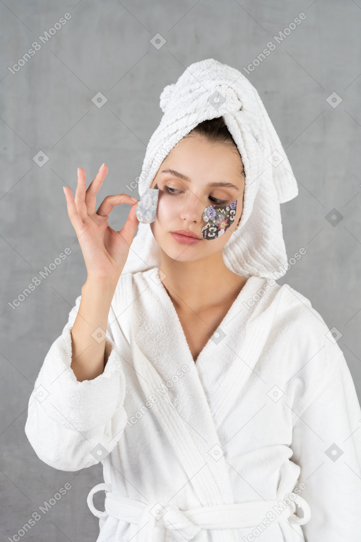 Mujer en bata de baño pelándose el parche en el ojo