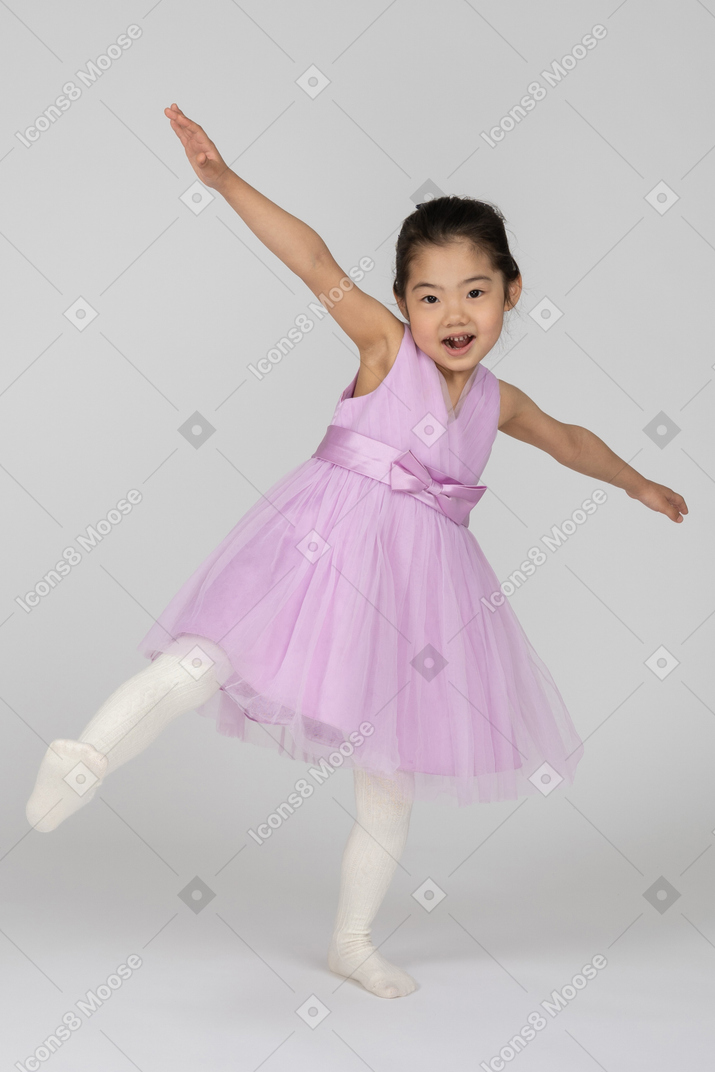 飛んでいるかのように彼女の腕を広げているピンクのドレスを着た幸せな女の子