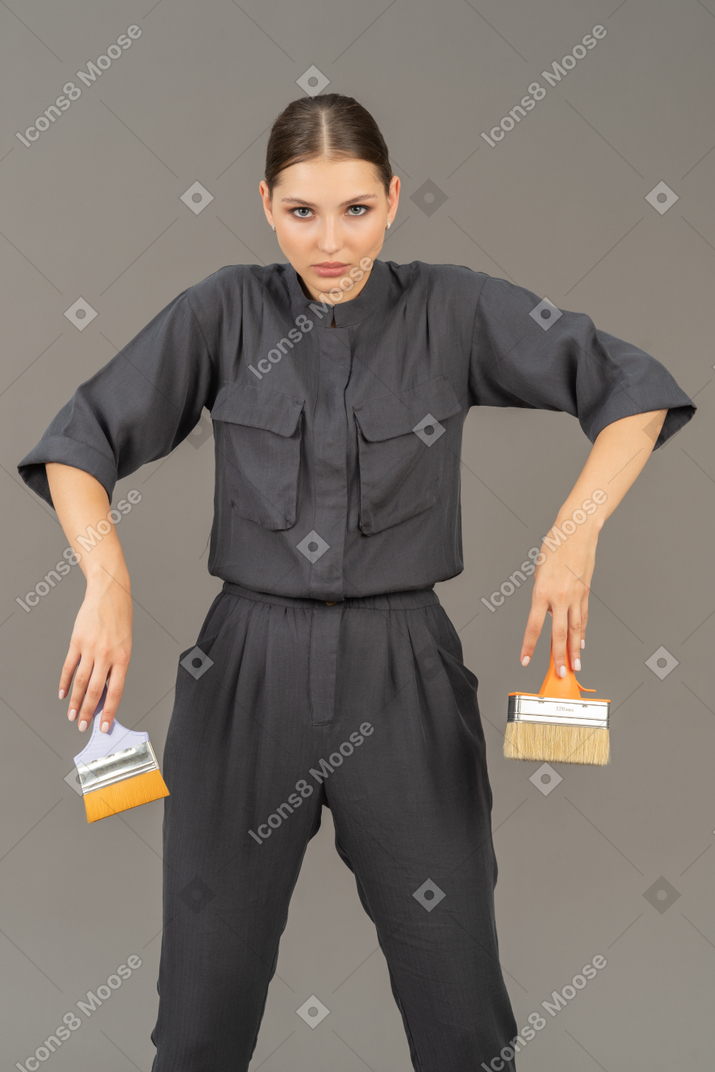 Woman in gray coveralls holding paint brushes