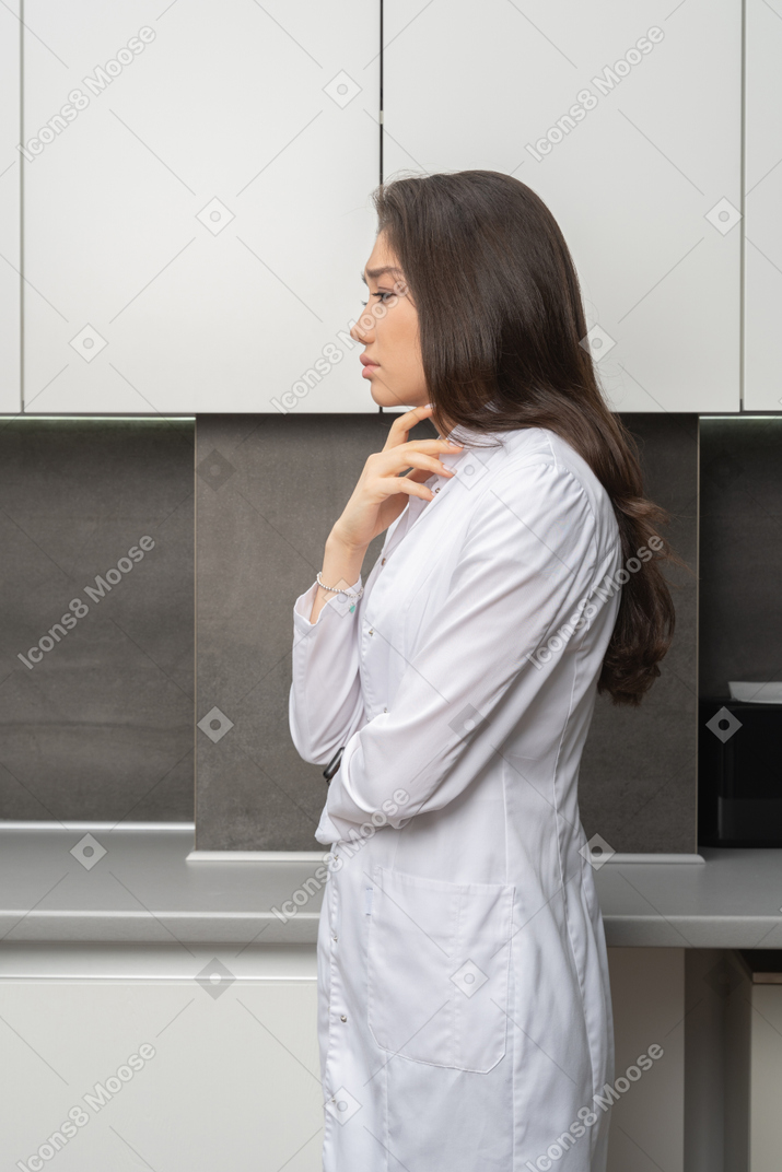 Side view of a doubtful female doctor touching chin