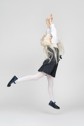 Side view of a schoolgirl jumping with hands up
