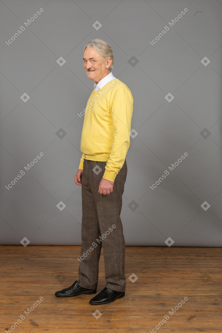 Vista de três quartos de um homem velho e alegre de blusa amarela, sorrindo e olhando para a câmera